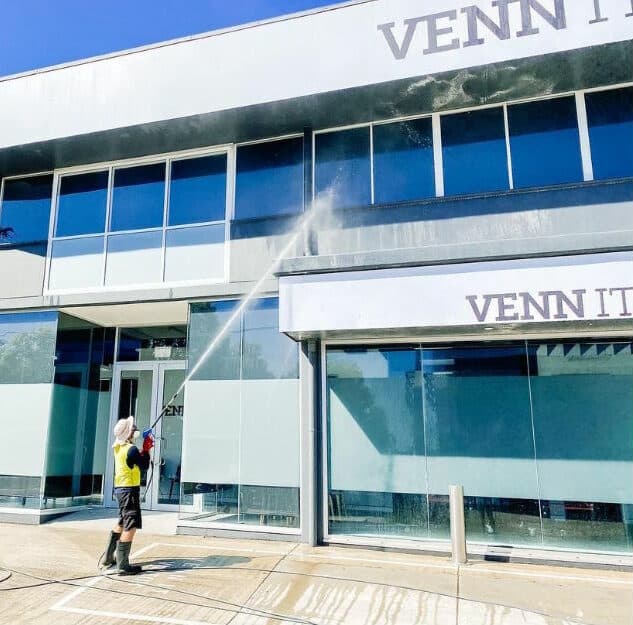 Worker soft washing the exterior of a commercial building